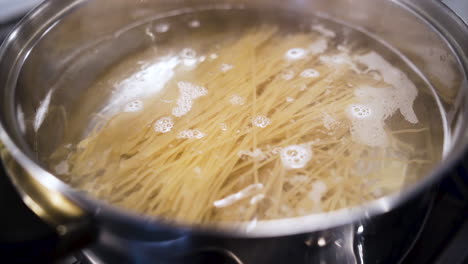 Dejando-Caer-Un-Puñado-De-Fideos-Espaguetis-En-Una-Olla-De-Agua-Hirviendo-En-Cámara-Lenta