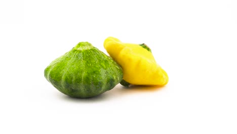 two pattypan squashes - green and yellow. rotating. isolated on the white background. close-up. macro.