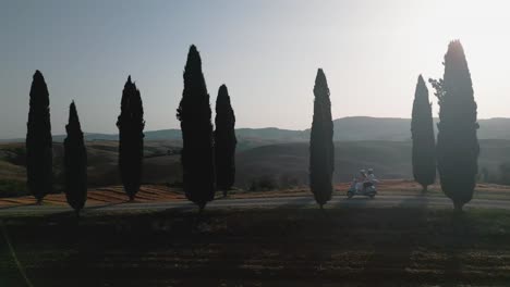 scooter rider passes through cypress trees on a scenic road in the rolling hills of tuscany at sunset