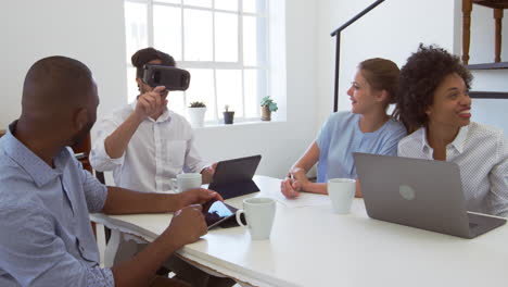 man in vr goggles at a desk with colleagues in an office