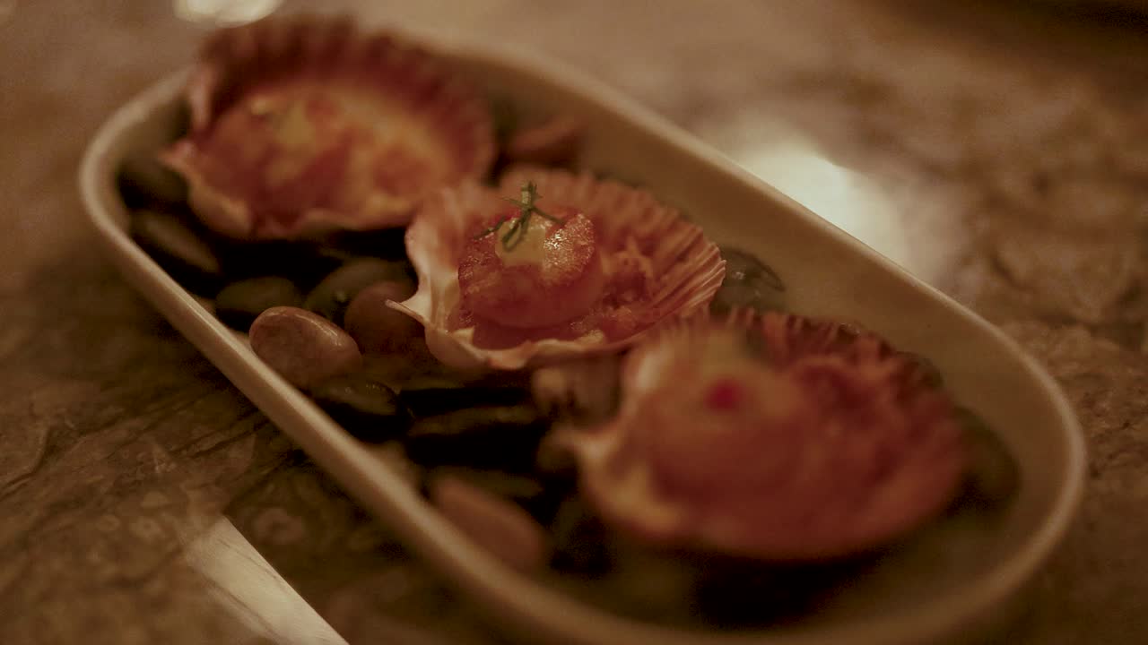 Grilled scallops presented on a decorative platter, captured in warm, ambient lighting with a focus on culinary artistry