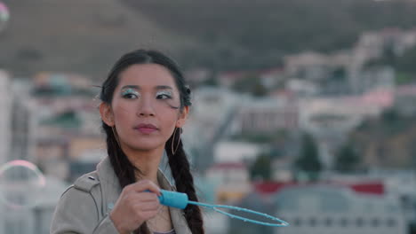 beautiful-young-asian-woman-blowing-bubbles-on-rooftop-at-sunset-enjoying-playful-summer-day-looking-curious-with-city-in-background