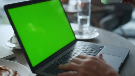 Manos-Del-Hombre-Escribiendo-Teclado-Computadora-Portátil-Pantalla-Verde-En-La-Mesa-Del-Restaurante-Cafetería.