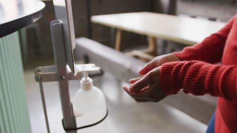 Midsection-of-african-american-woman-working-at-a-bar,-using-hand-sanitising-gel-dispenser