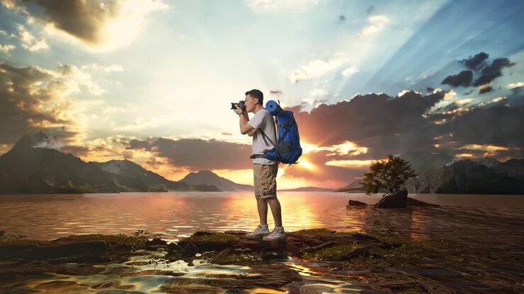 Full Body Side View Of Asian Male Hiker With Mountaineering Backpack Using A Camera Taking Picture At A Lake