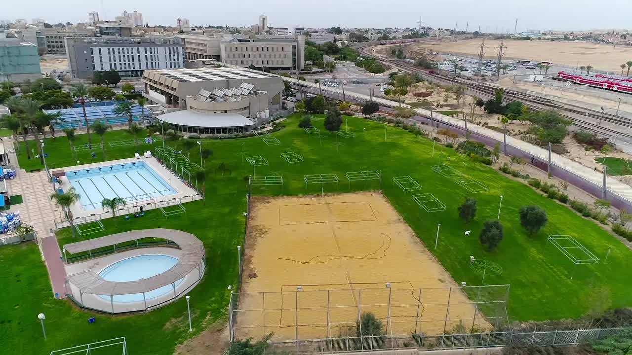 Take drone aerial over a pool area and sports spaces.