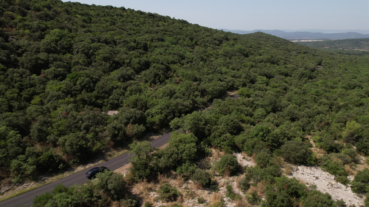 vista lateral aérea disparado coche eléctrico conduciendo en una carretera con bosque alrededor soleado