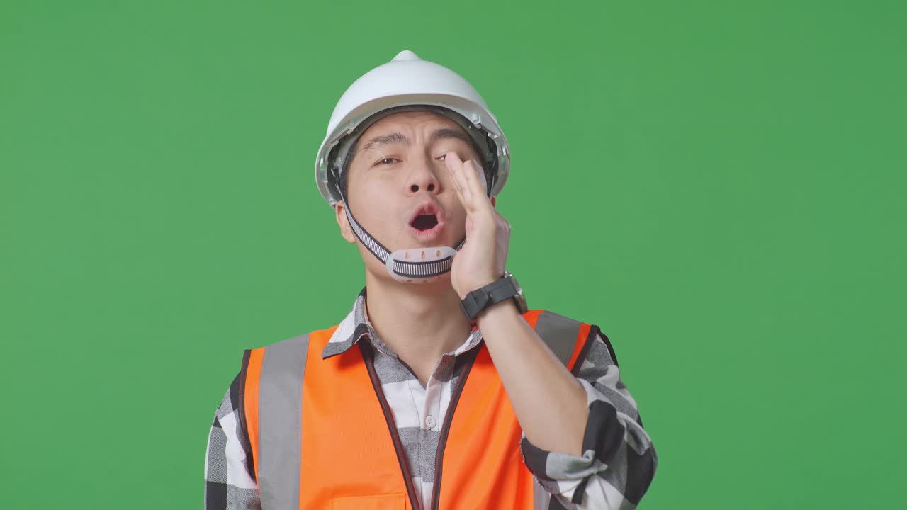 Close Up Of Asian Male Engineer With Safety Helmet Yelling With Hand Over Mouth While Standing In The Green Screen Background Studio