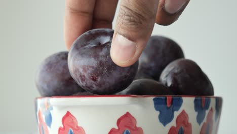 hand picking plums from a bowl