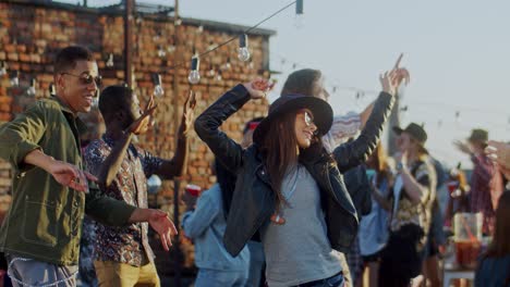Beautiful-Stylish-Youg-Girl-In-A-Hat-And-Dark-Sunglasses-Dancing-Joyfully-With-Her-Friends-At-The-Rooftop-Party