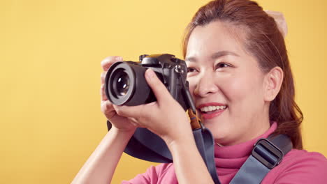 광고용 카피 공간이 있는 고립된 노란색 배경에 디지털 카메라를 사용하여 분홍색 옷을 입고 노는 젊은 아시아 여성-1