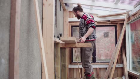 hombre arreglando una tabla de madera, construyendo un invernadero - toma amplia