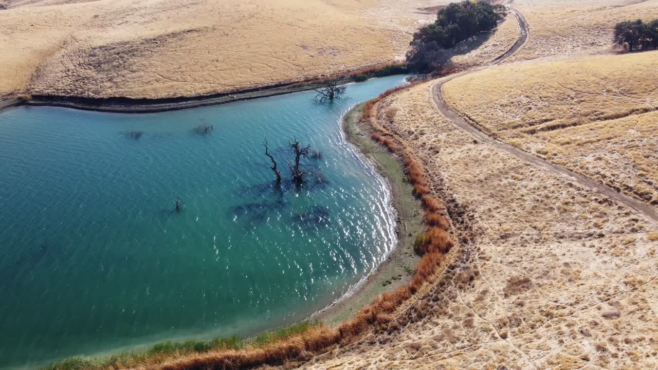 Moving drone footage of stunning blue water surrounded by golden rolling hills