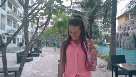 long haired girl with drink in hand walks at hotel smiling