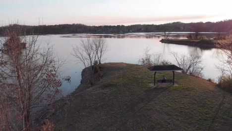 drone footage flying over a point of land over the lake with a swing and someone sitting in it below at sunset