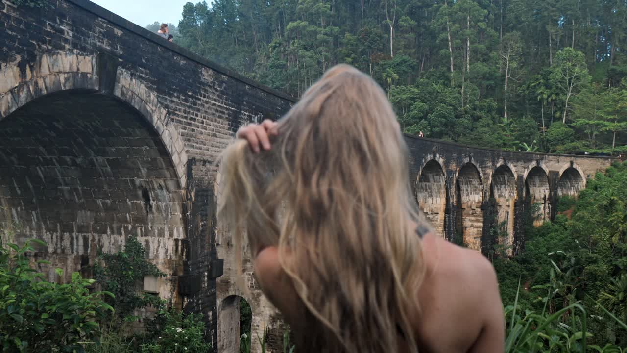 A young woman observes the historic Nine Arch Bridge from a nearby hillside in Ella, Sri Lanka.