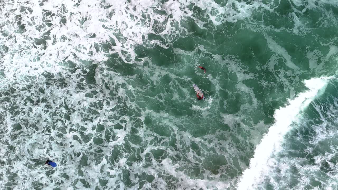 Aerial, birds eye view shot of surfers and colourful surfing boards enjoying the large waves with white caps