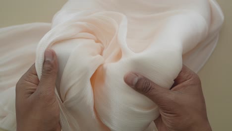 hands holding a piece of light peach colored fabric