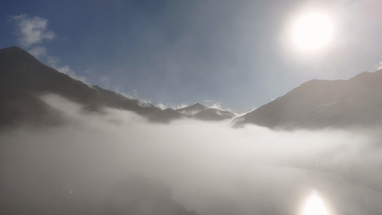 Aerial view of mist-covered mountains in Queenstown, New Zealand, during sunrise. Crisp winter air and clear skies enhance the serene atmosphere