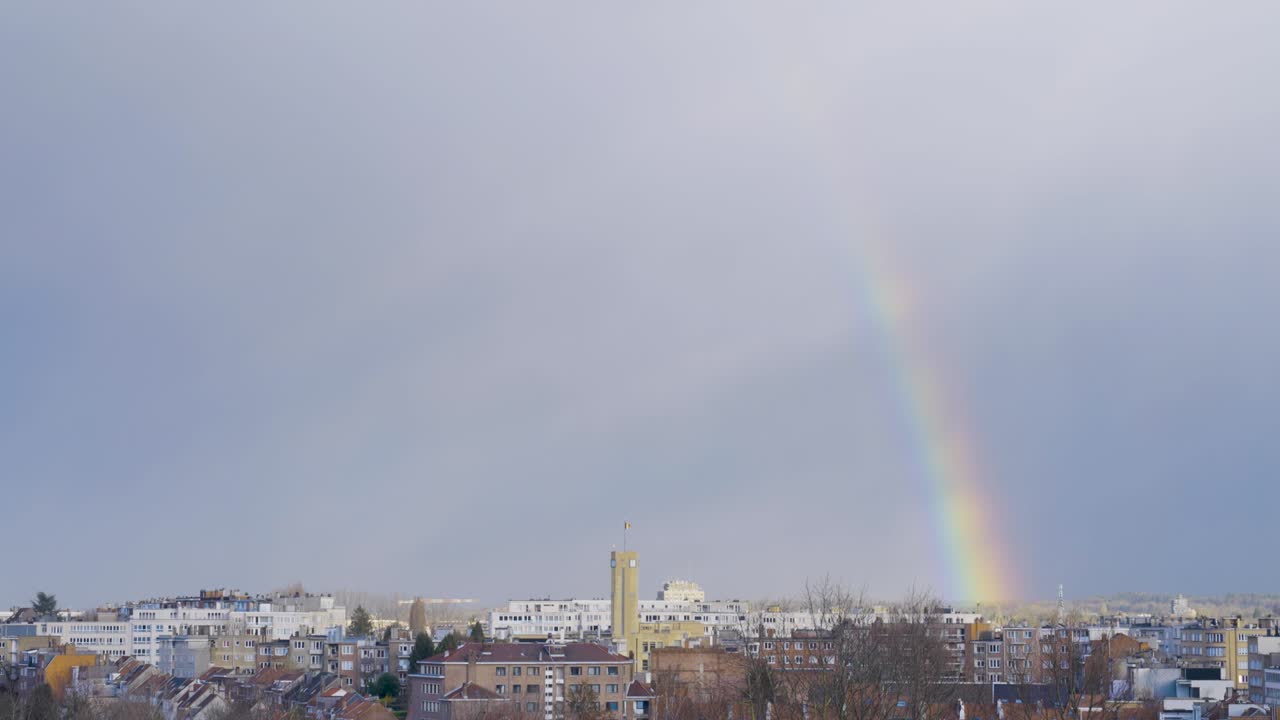 bandera belga ondeando en la parte superior del ayuntamiento de woluwe-saint-lambert en bruselas, bélgica, arco iris que se desvanece en el fondo del cielo nublado