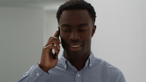 close up of smiling young businessman walking along corridor in office talking on mobile phone