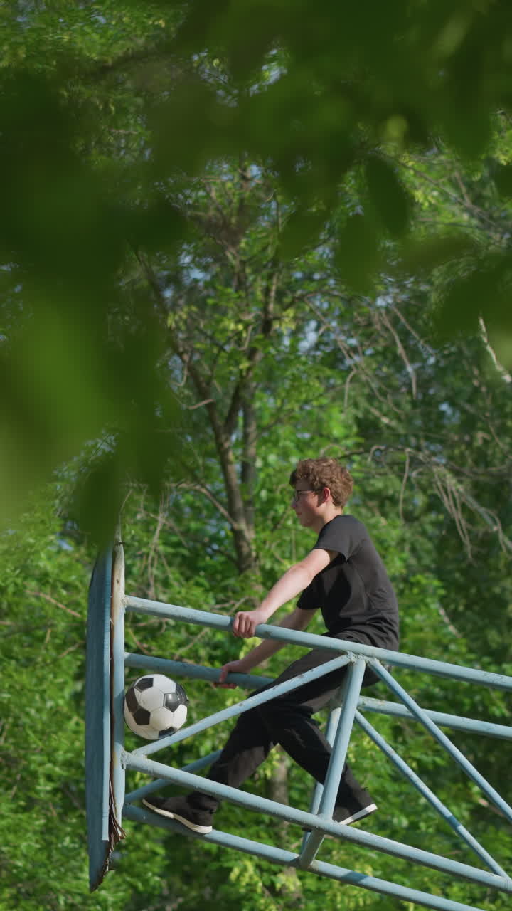 un niño se sienta centrado en el equipo al aire libre de hierro azul, agarrando ambos lados del hierro, mientras una pelota permanece atascada en el marco