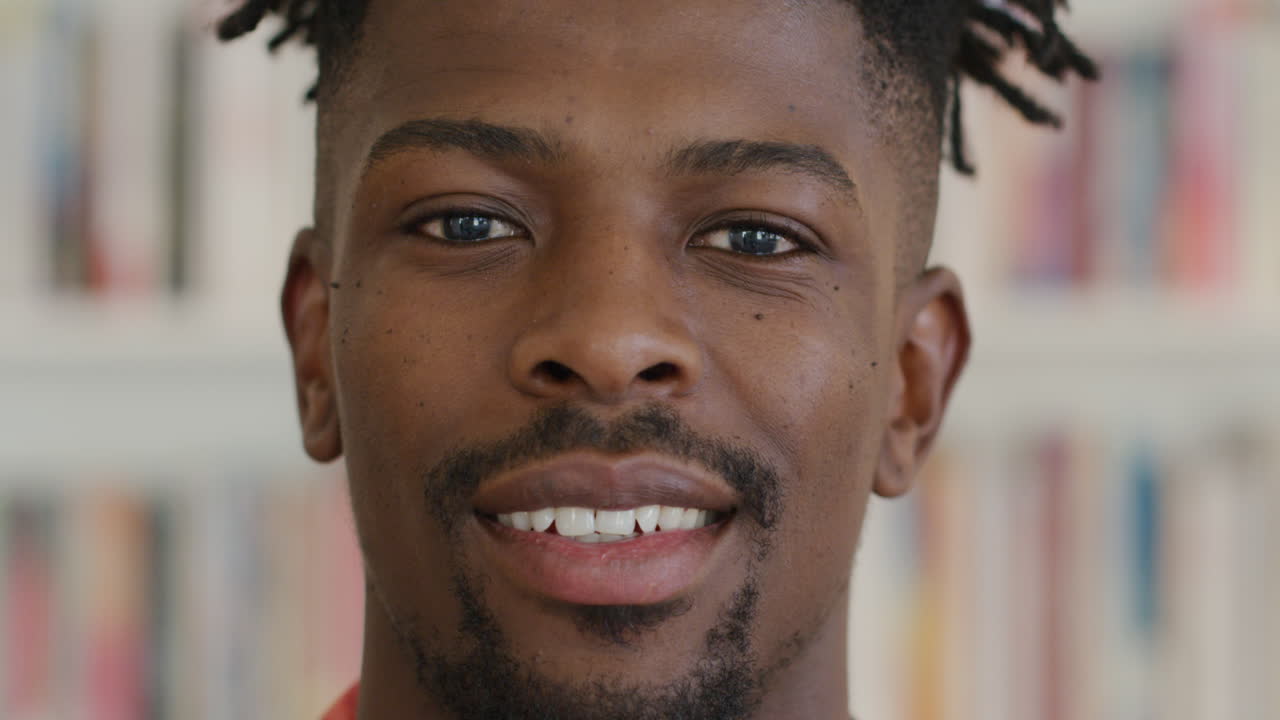 retrato de un feliz estudiante afroamericano sonriendo frente a una estantería de libros en la biblioteca de la universidad