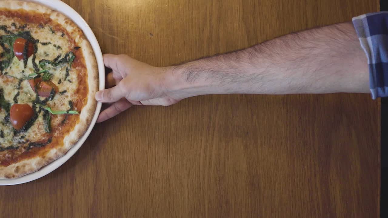 persona deslizando una pizza fresca sobre una mesa de restaurante de madera con solo una mano y un brazo visibles