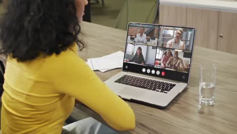 Biracial-woman-using-laptop-for-video-call,-with-diverse-business-colleagues-on-screen