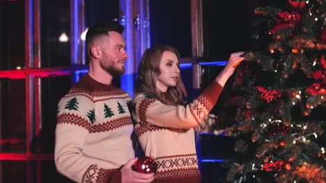 young couple decorates christmas tree. young family in christmas sweaters prepares for new year celebration at home. portrait of beautiful family pair near new year tree.