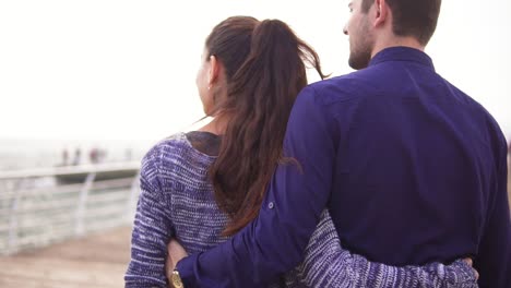 close-up back view of young beautiful couple walking by the sea, talking and embracing each other. woman is pointing at