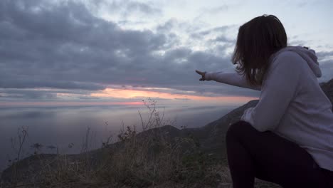 girl squat on a high cliff and watch the sunset through cloudy sky over adriatic sea-2