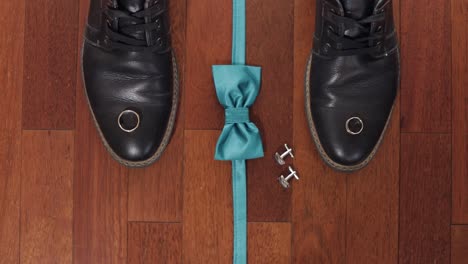 Wedding-rings,-green-grooms-bow-tie,-cufflinks-and-shoes-on-brown-wood-floor