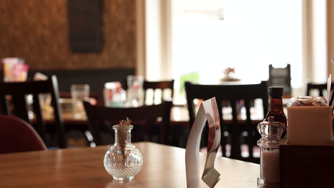 Camera slowly pans across a sunlit restaurant table, highlighting condiments and cozy interior details