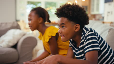 brother and sister sitting on sofa at home playing video game together with girl winning