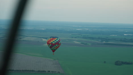 distant view of colorful hot air balloon drifting over patchwork farmland under pale sky at dusk showcasing serene aerial panorama and silent drifting adventure with distant horizon