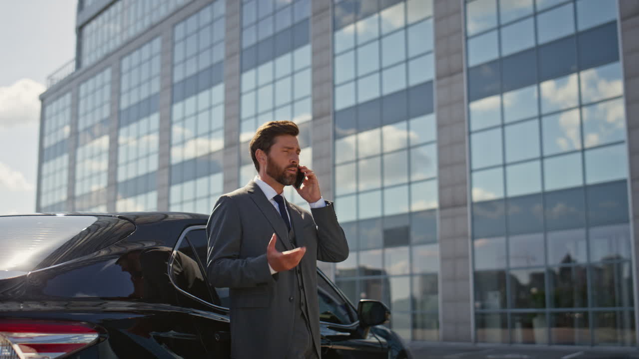 Primo piano di un CEO preoccupato che parla allo smartphone vicino a un'auto di lusso in una strada soleggiata.