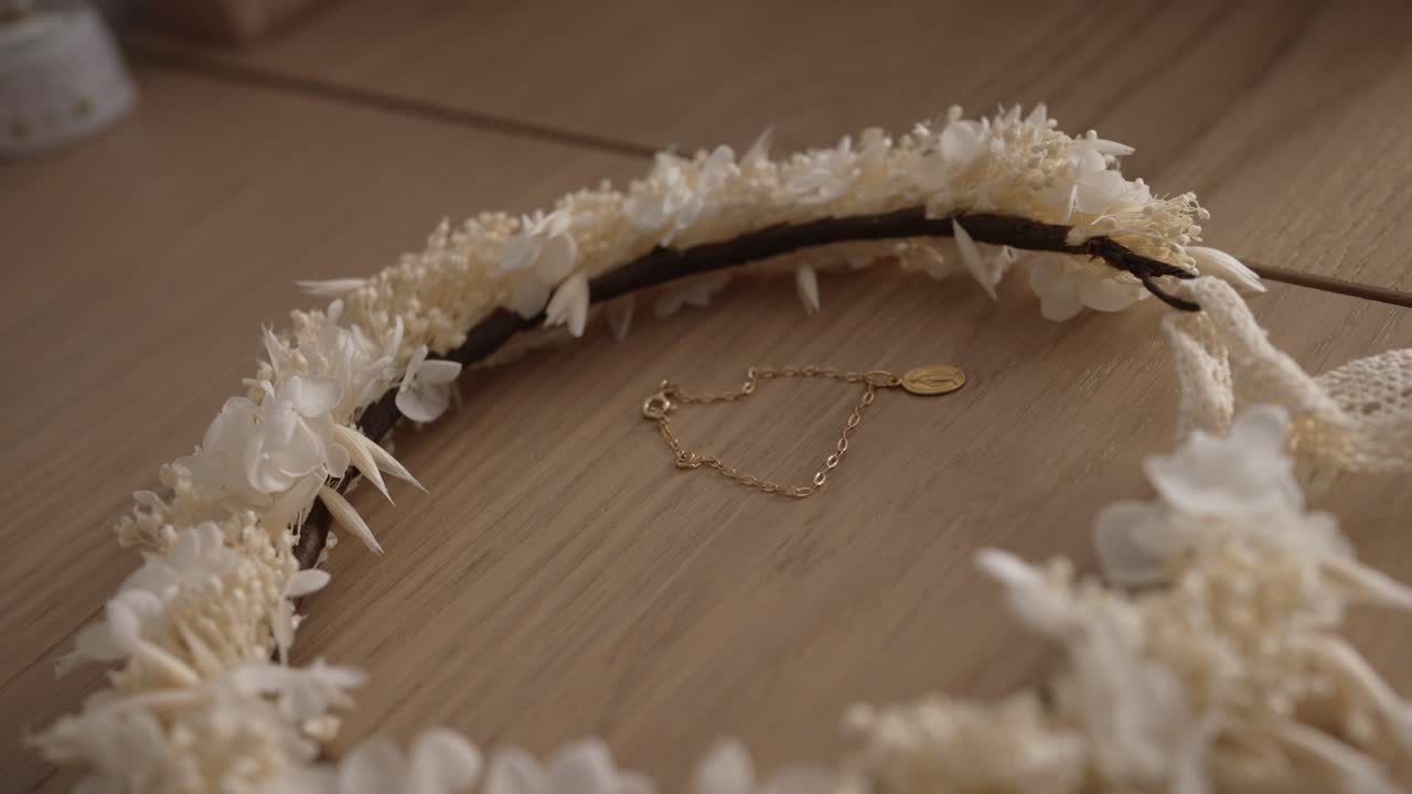 close up of small gold bracelet and white flower crown on wooden table in soft natural light