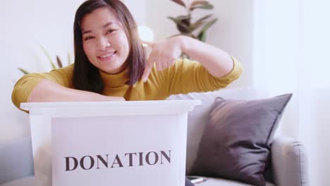 lovely woman pointing to box with donations, inviting others to donate too