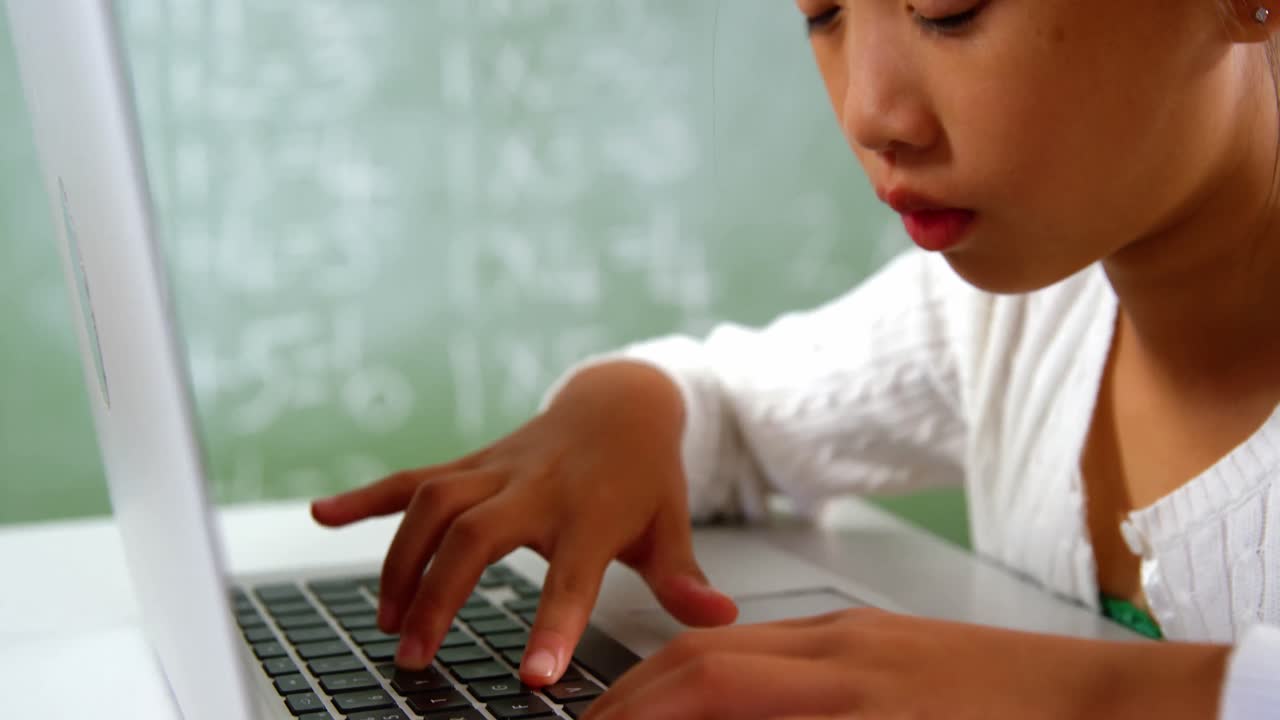 Schoolgirl using laptop in classroom