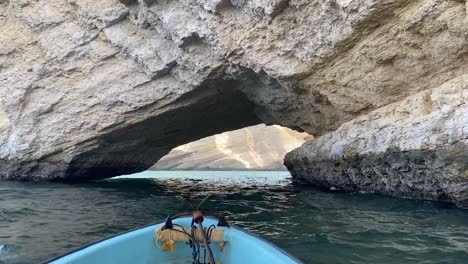 a ship with an anchor slowly passes under a natural stone arch near qantab beach in muscat, oman