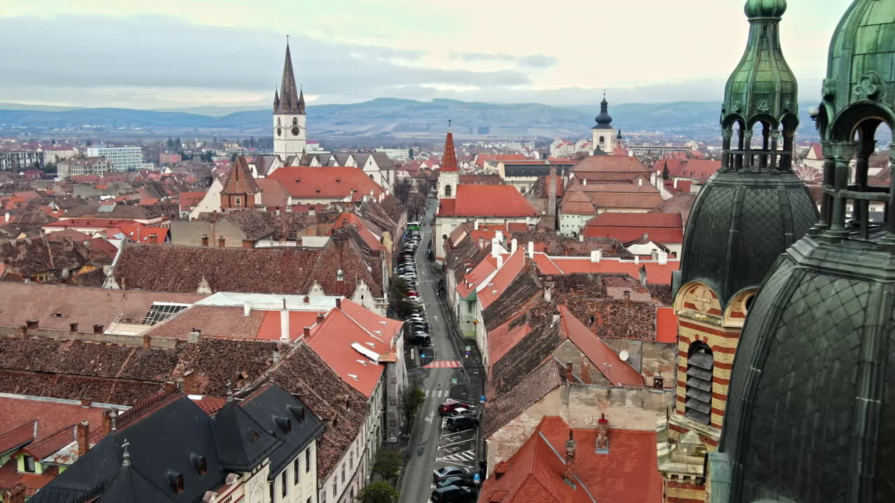 Aerial drone view of the Sibiu Lutheran Cathedral in Romania. Street with cars and bare trees, multiple buildings, cityscape
