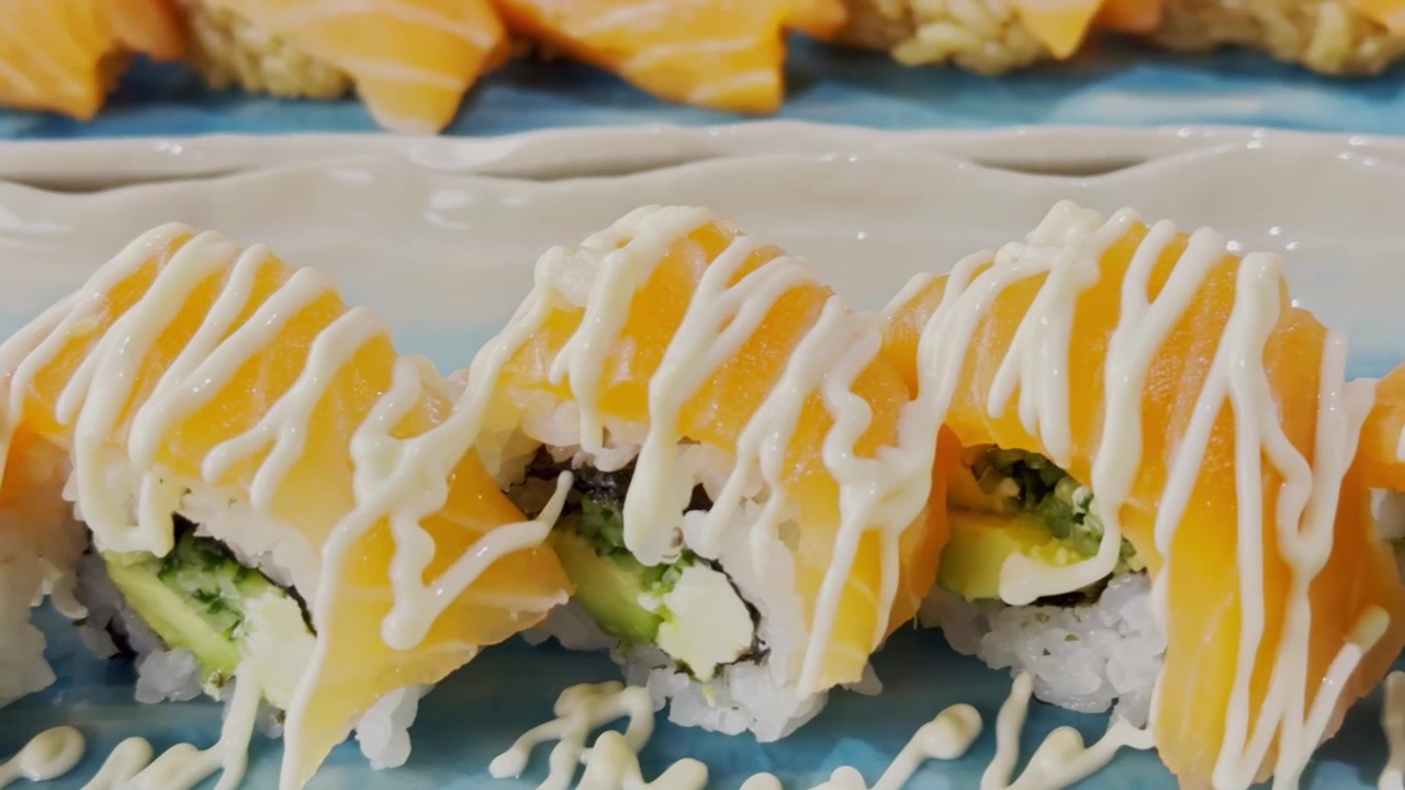 Lähikuva California roll -sushista aseteltuna tarjoilulautaselle, sisältäen riisiä, mereneläviä, avokadoa ja tuoreita ainesosia elegantilla esillepanolla