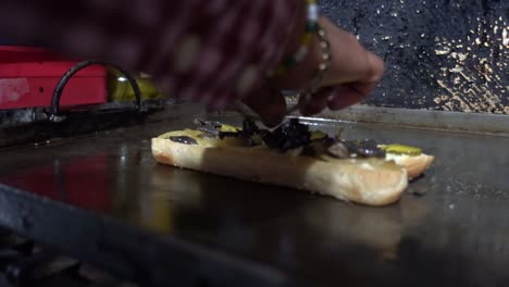 disparo en primer plano de un chef agregando aderezos a un pan de perrito caliente cocinando en la parrilla