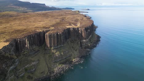 Aerial-drone-panning-shot-of-the-high-Kilt-Rock-in-Scotland-on-a-sunny-day-at-the-calm-ocean