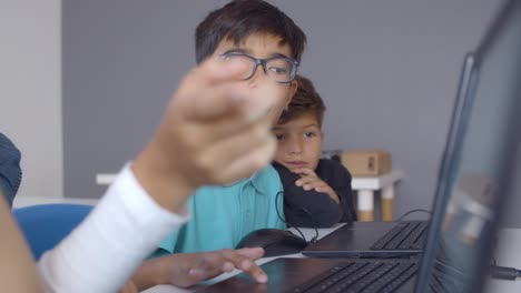 focused schoolboy in glasses helping classmates to do task