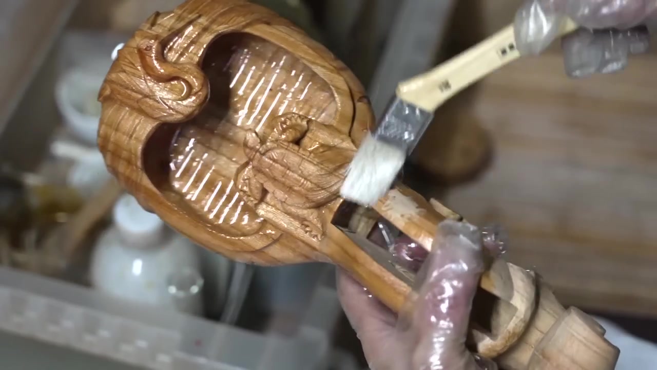 Artesano aplicando laca a un tintero de madera intrincadamente tallado para resaltar su acabado ámbar profundo