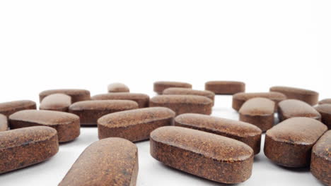 close-up of multiple herbal supplement pills scattered on white background