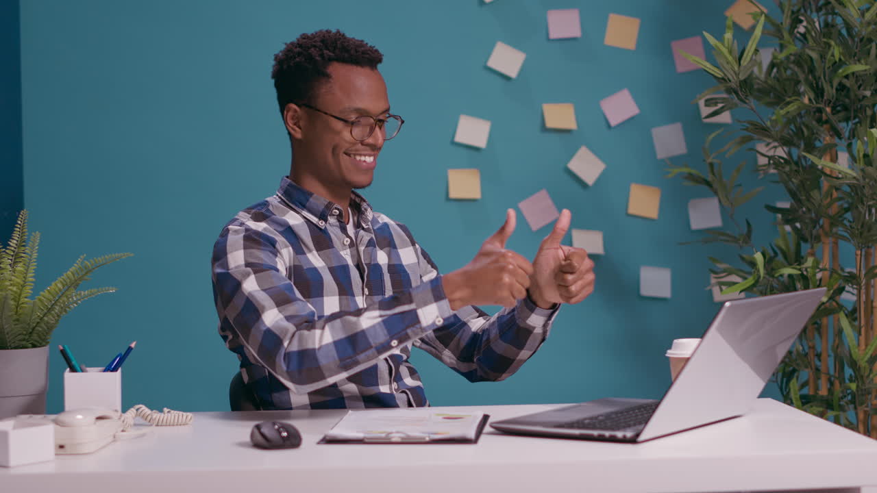Cheerful person showing thumbs up gesture in front of laptop screen