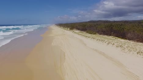 smooth and slow rising aerial drone shot looking south over the dunes and bushland, down a deserted main beach, on north stradbroke island in sunny queensland, australia